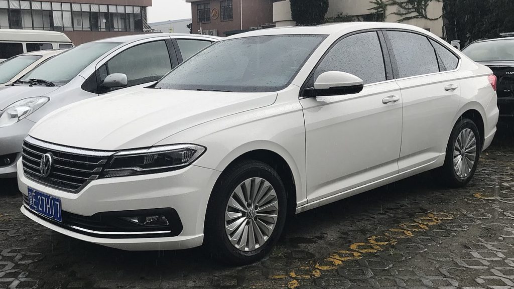 Carro branco estacionado em área pavimentada sob tempo chuvoso.