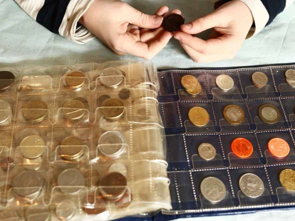 Livro repleto de moedas embaladas em plástico, como se fosse uma coleção de unidades monetárias organizadas. Com uma mulher segurando uma moeda en suas mãos e a analisando.