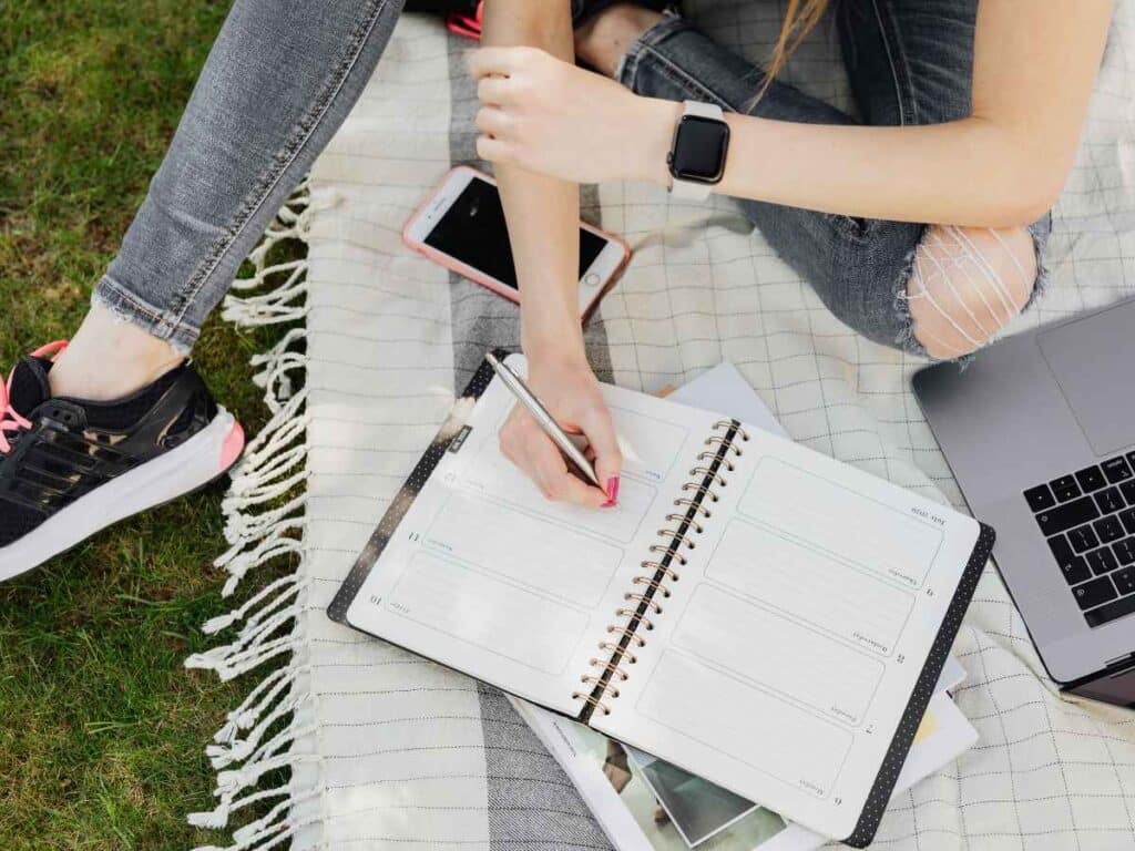 Menina sentada na grama enquanto se planeja para estudar redação.