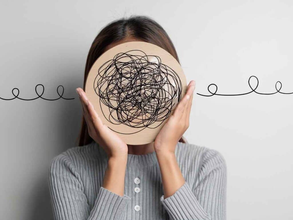 Mulher cobrindo o rosto com uma placa desenhada com rabiscos confusos, simbolizando confusão mental