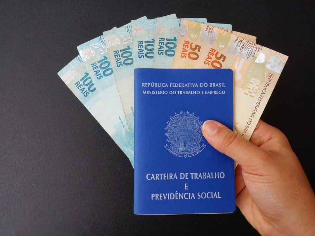 Funcionário segurando uma carteira de trabalho junto ao salário recebido, que já inclui as contribuições ao Fundo de Amparo ao Trabalhador (FAT). Fundo preto sólido.