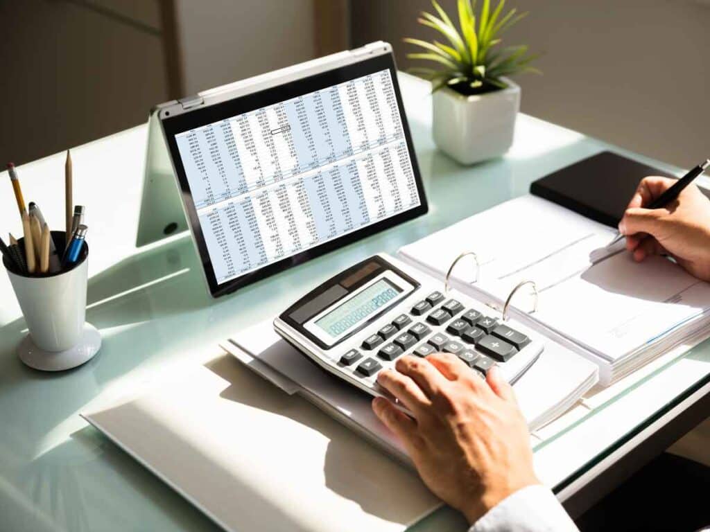 Funcionário analisando possíveis irregularidades em seu registro na carteira de trabalho e no FGTS. À sua frente, um tablet exibe informações detalhadas, enquanto ele utiliza uma calculadora e faz anotações para verificar inconsistências.