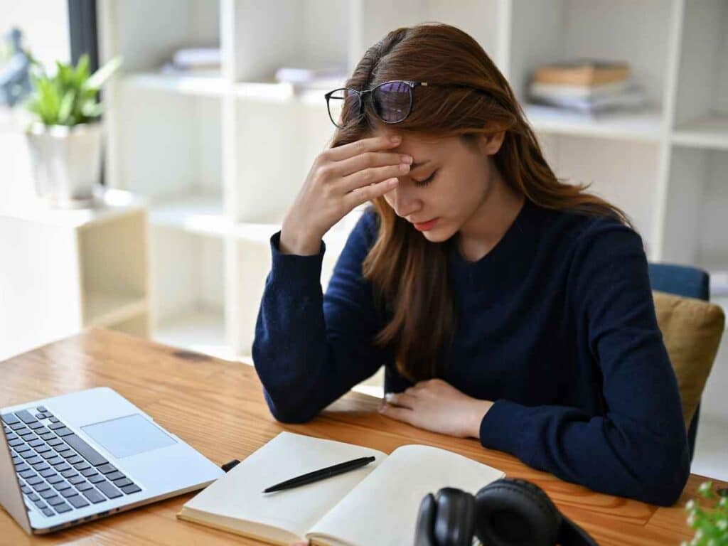 Profissional sentada em frente ao computador, com o cotovelo apoiado na mesa e a mão segurando a cabeça, expressando frustração por ter perdido o prazo de solicitação do seguro-desemprego.