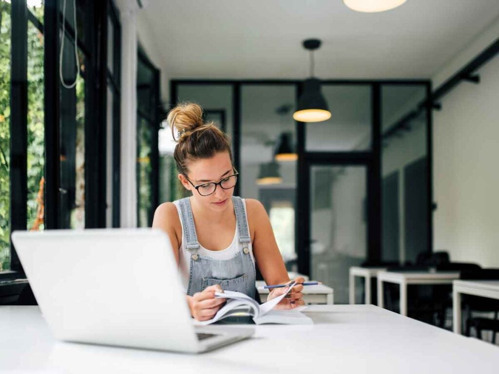 Mulher estudando a formação das palavras compostas, em especifico os dias da semana. Ela lê suas anotações sobre as regras do acordo ortográfico.
