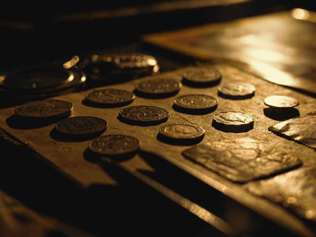 Moedas comemorativas organizadas em uma superfície, iluminadas por uma luz amarelada e suave, destacando seus detalhes em relevo. A imagem remete a uma coleção de tiragem limitada, valorizando a exclusividade e o apelo histórico desses exemplares.