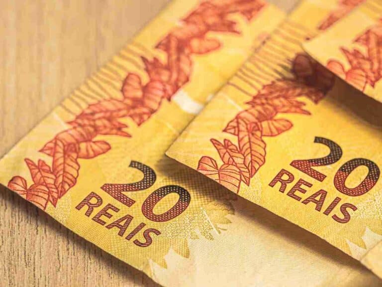 Cédula de 20 reais sobre uma superfície de madeira, destacando detalhes da cor amarela vibrante e elementos gráficos em tons avermelhados.