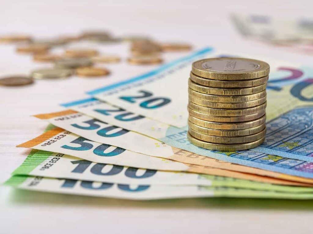 Montagem com cédulas organizadas em leque, com valores de 20, 50 e 100, acompanhadas por uma pilha de moedas ao centro.