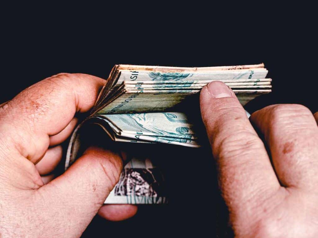 Mãos folheando um maço de cédulas de real, com atenção aos detalhes das notas, sugerindo a busca por cédulas raras ou valiosas para coleção.