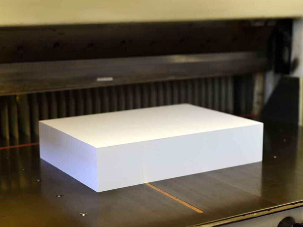 Resma de papel branco posicionada sobre uma mesa metálica em ambiente corporativo ou industrial. A imagem destaca a uniformidade e o volume do bloco de folhas