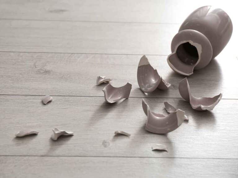 Vaso de cerâmica quebrado em vários pedaços sobre um piso claro de madeira.