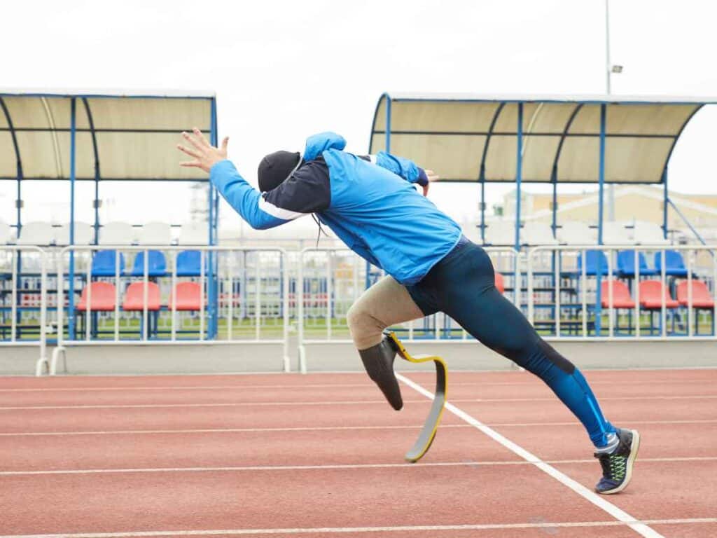 Atleta paralímpico com prótese correndo em pista de atletismo.