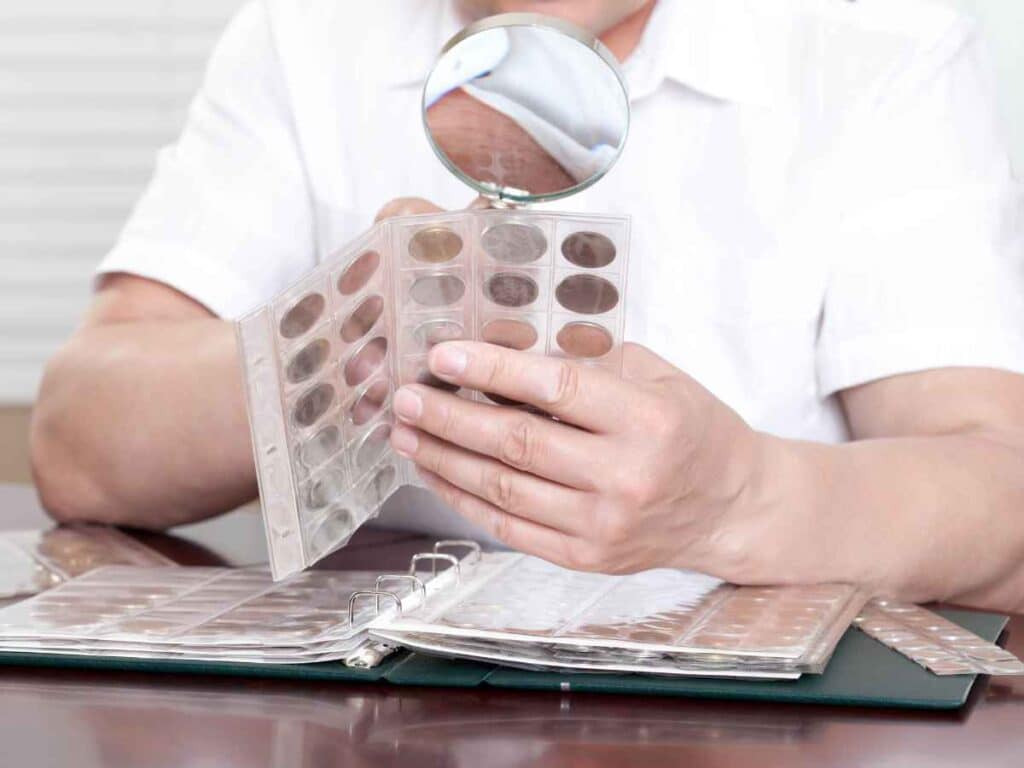 Pessoa examinando moedas com lupa e álbum de colecionador, representando a prática de identificar e vender moedas raras com valor histórico e comercial.