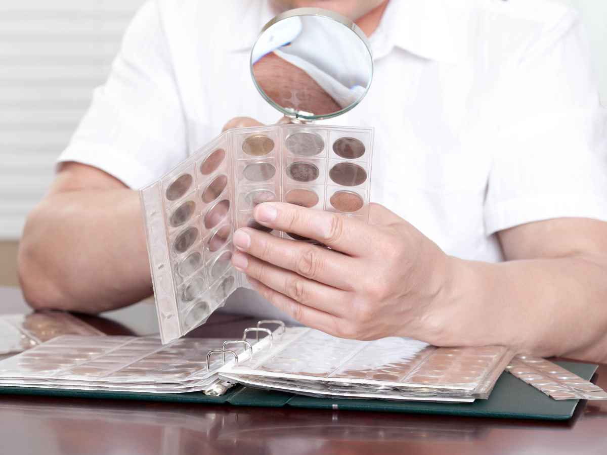 Pessoa examinando moedas com lupa e álbum de colecionador, representando a prática de identificar e vender moedas raras com valor histórico e comercial.