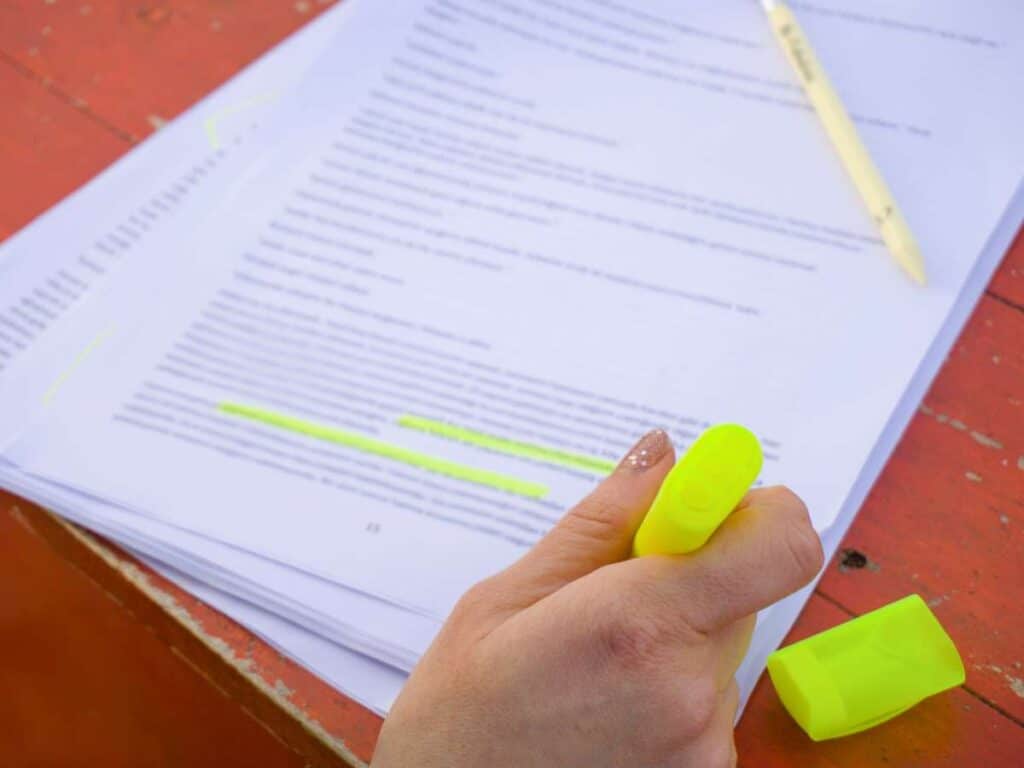 Mão de estudante destacando informações importantes em um texto com marca-texto amarelo durante estudo.