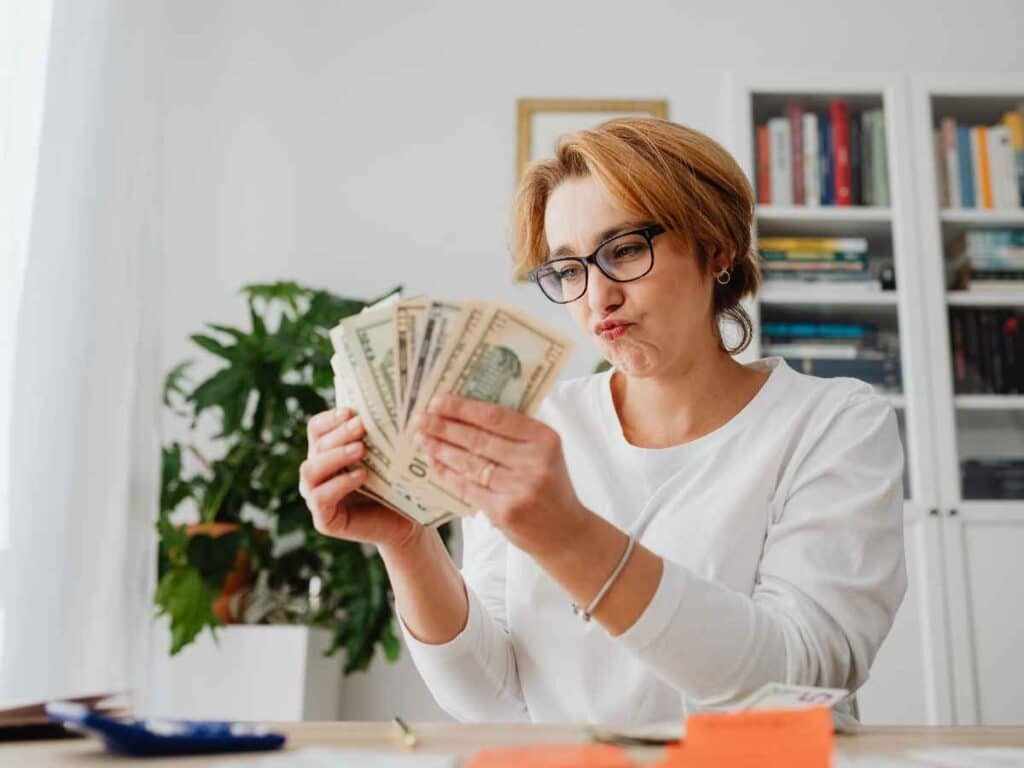 Mulher com expressão concentrada procurando notas de dois reais em casa