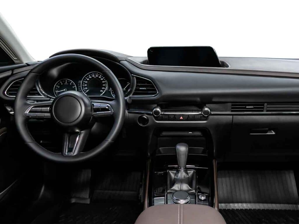 Painel interno de um carro moderno visto de frente, com volante, câmbio automático e painel digital iluminado.