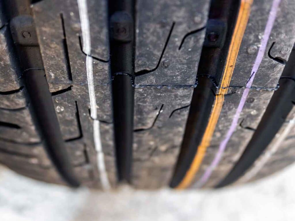 Close-up do sulco de um pneu de carro mostrando os detalhes da banda de rodagem e as linhas coloridas indicativas de fabricação, destacando o estado de conservação e a profundidade